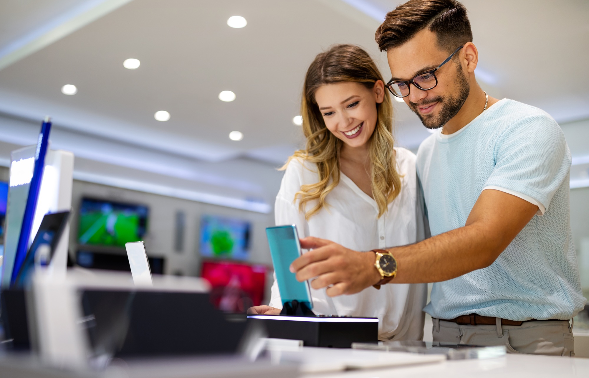 Smiling couple exploring new tech at a modern showroom, interacting with a tablet—capturing the shopping experience at a Tablets and Mobile Devices Store
