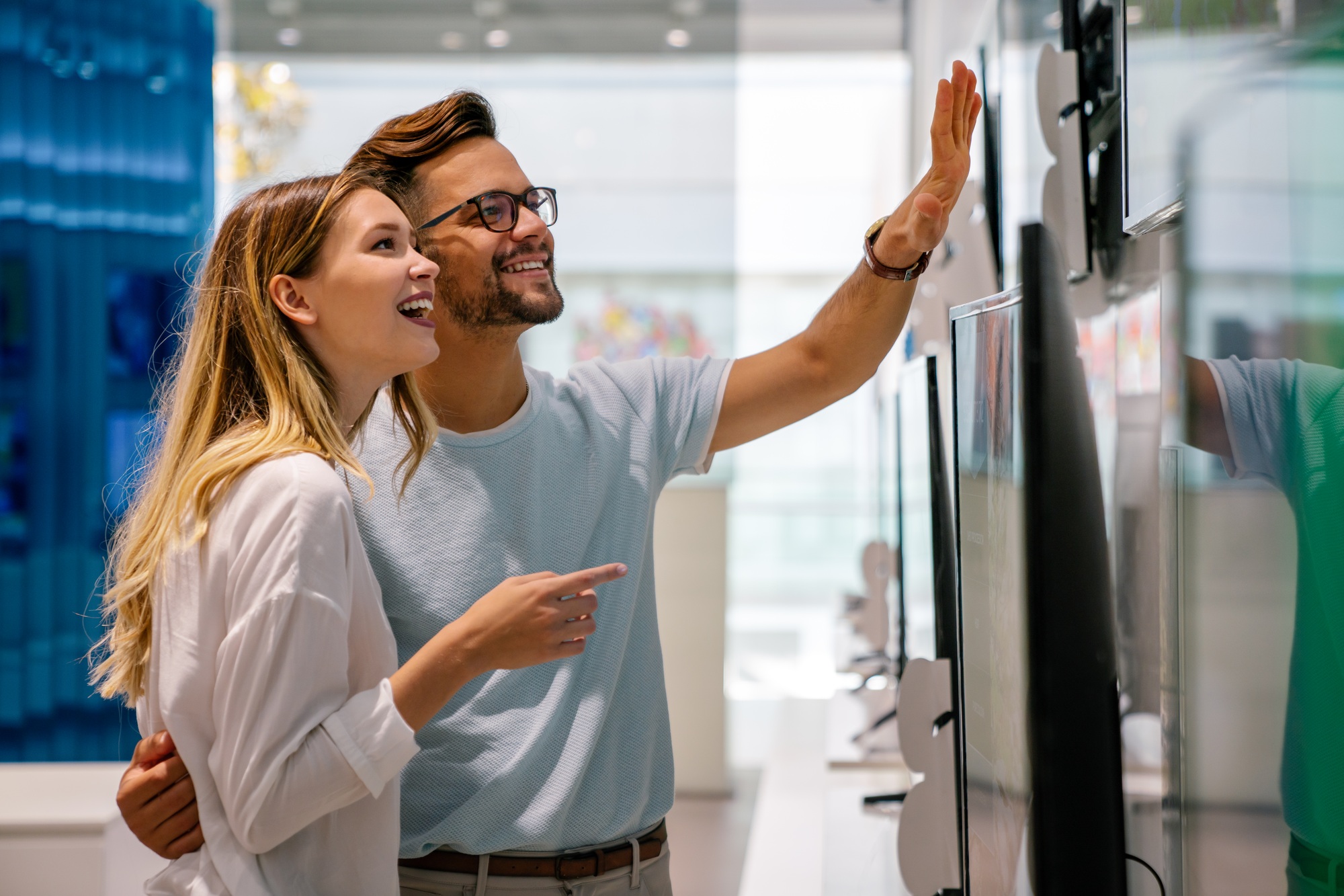 Excited couple exploring TV options in a sleek electronics store, discovering Hot Tech Deals UnitedTech offers on the latest screens. 