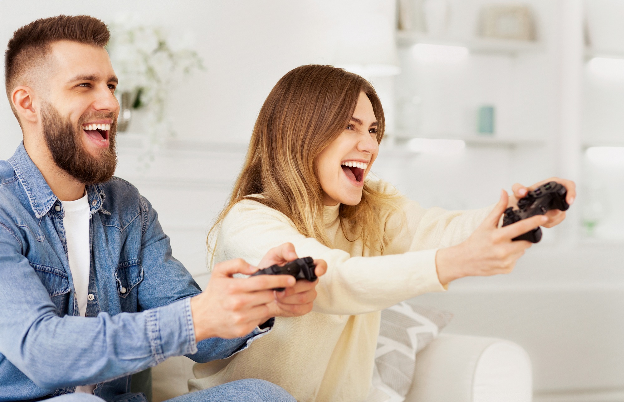 Happy couple playing video games at home using dual wireless controllers—showcasing product excitement for gaming controllers for sale at UnitedTech Deals.
