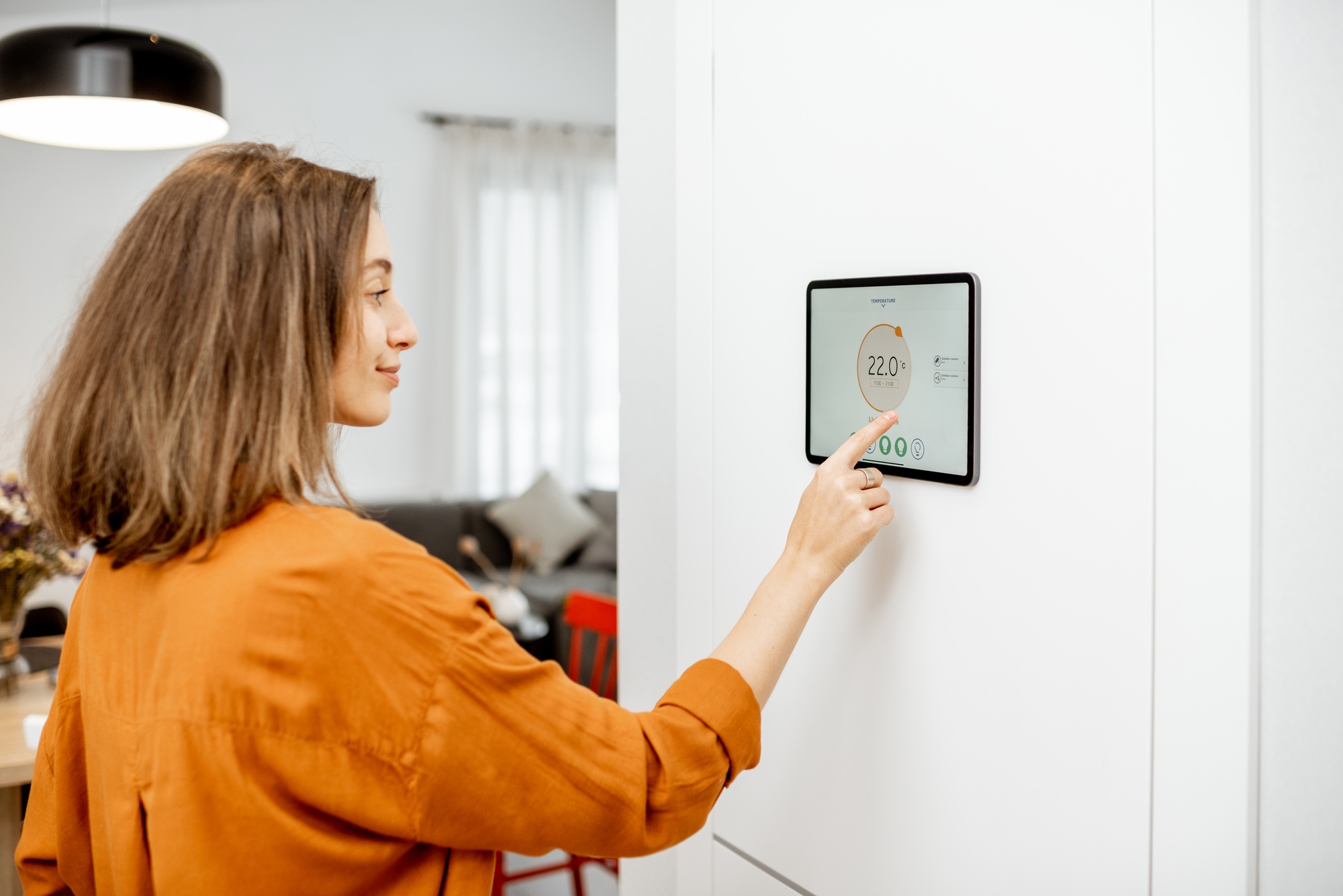 Woman adjusting home temperature on a wall-mounted smart display—perfect example of why customers buy smart displays Florida for modern living convenience.

