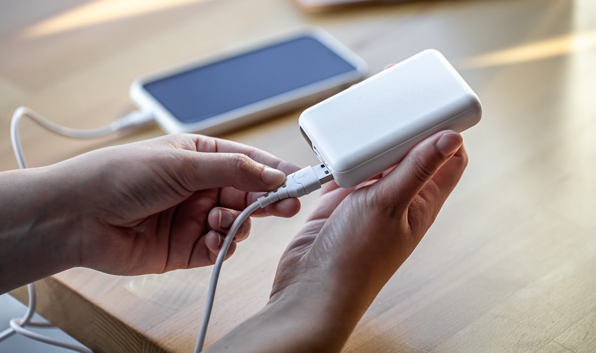 Customer plugging a charging cable into a portable power bank with a smartphone in the background—perfect visual representation for a cables and adapters store showcasing essential mobile accessories.