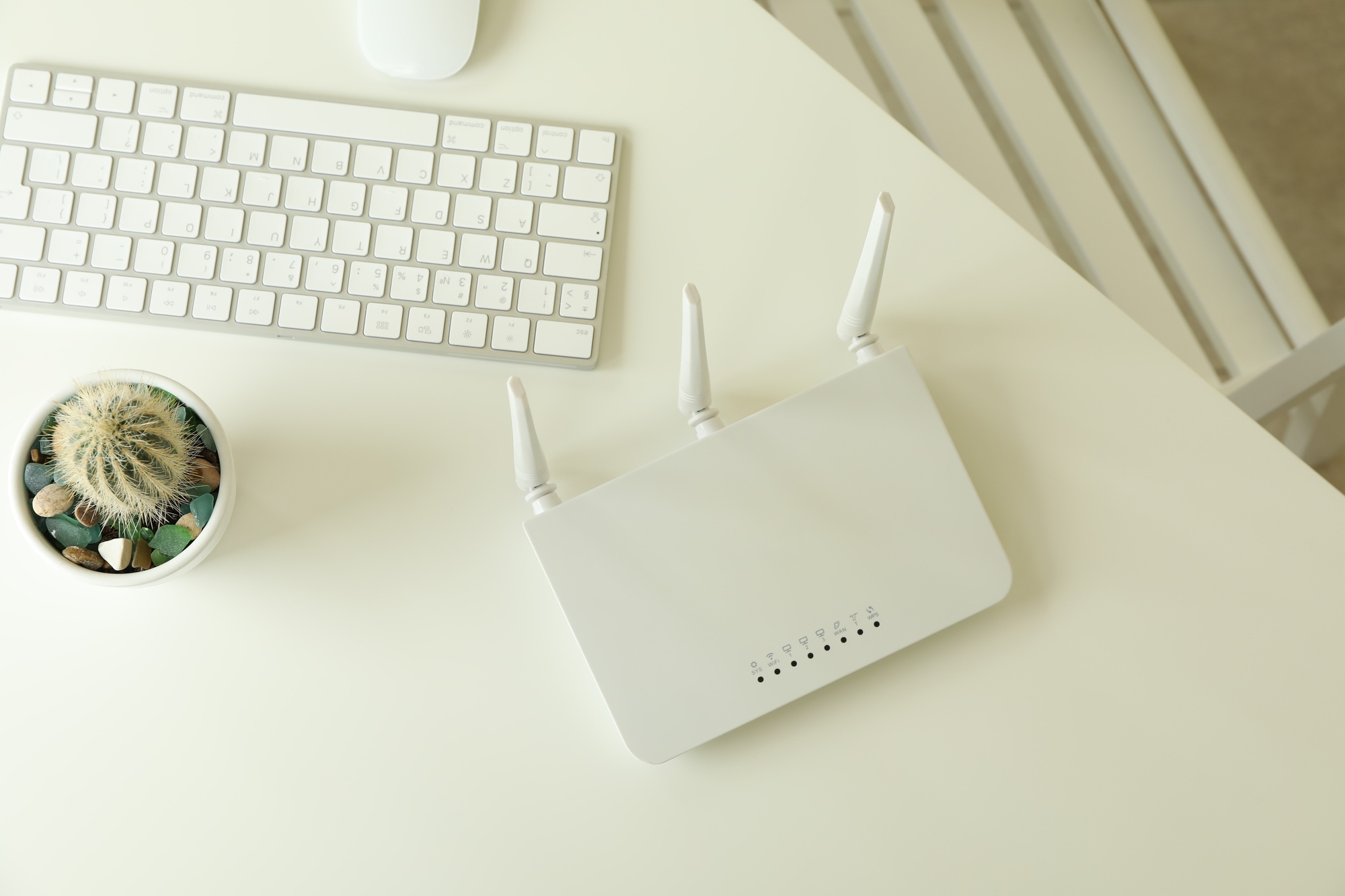 A modern white WiFi router with triple antennas placed on a clean desk beside a keyboard and cactus, representing reliable tech solutions to buy WiFi routers Florida.

