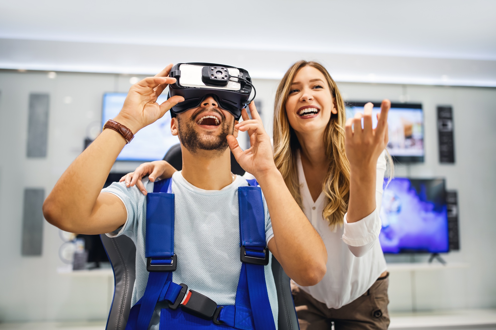 Excited man using a VR headset with a smiling woman beside him in a tech store—immersive experience highlighting why you should Buy VR Games Online today.